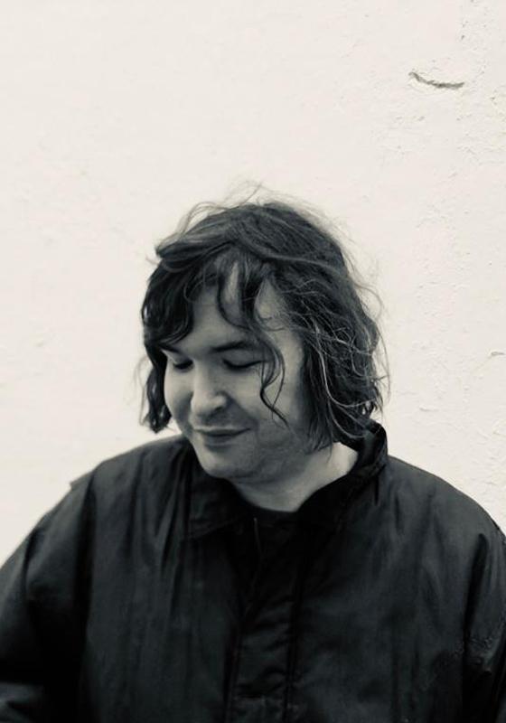 Monochrome headshot of Johnny against a white wall looking down.