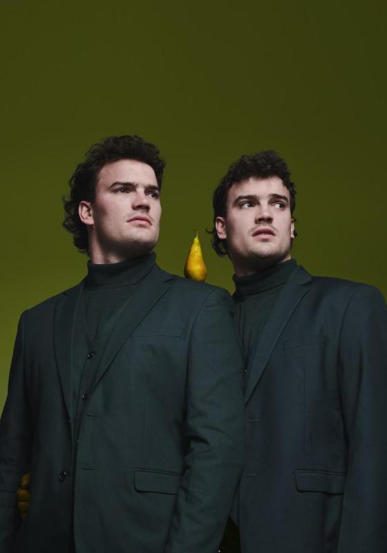 The twins in matching outfits with a pear on a shoulder.
