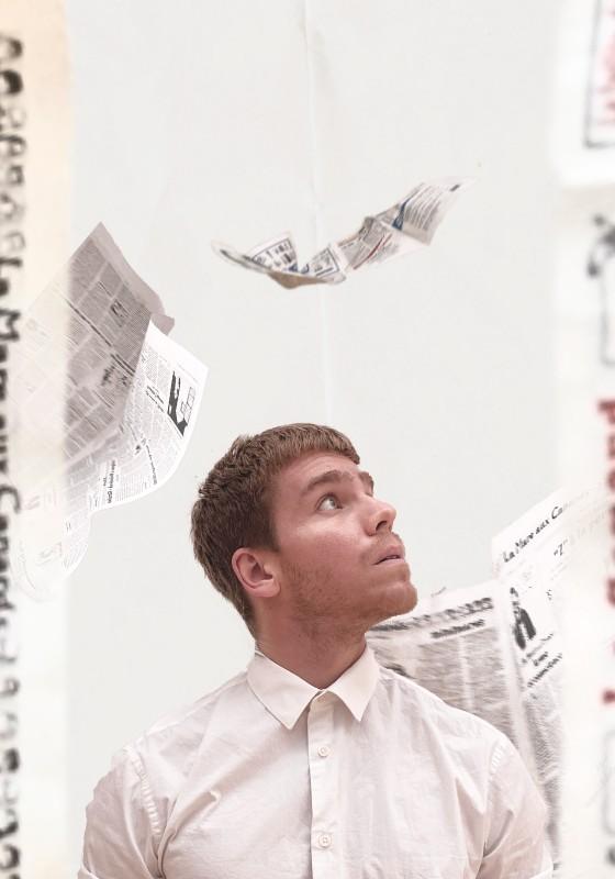 A man looks up quizzically whilst newspapers fall around him.