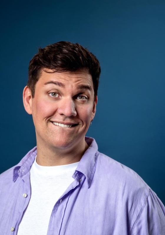 Dane grinning cheekily at the camera with a plain blue backdrop