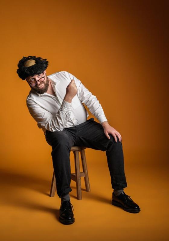 John Kearns wearing a wig and fake teeth sat on a stool.