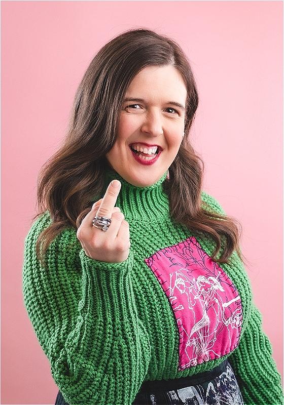 Photo of a smiling Rosie Jones swearing and sticking their middle finger up.