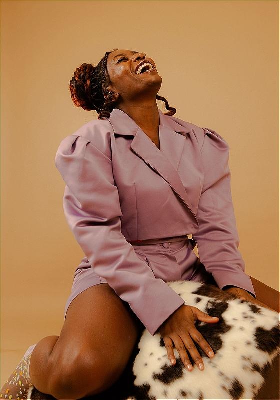 Sophie's head recoils back in laughter against a soft orange backdrop wearing a nice oversized coat