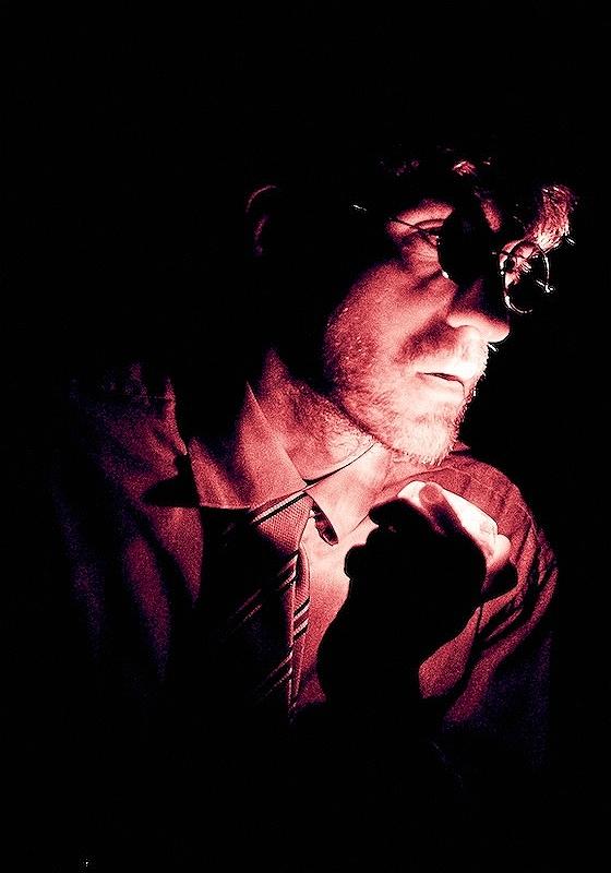 Side on shot of Joseph's face wearing circle rimmed glasses in stark edgy lighting looked befuzzled