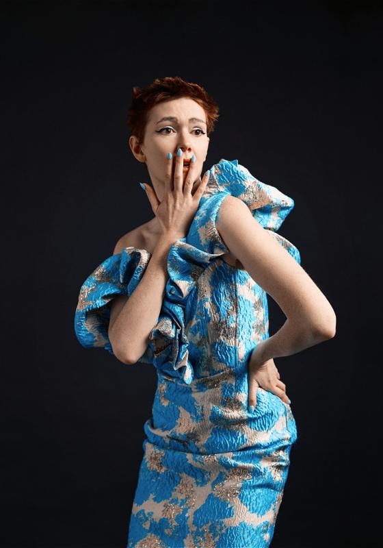 Elf stands majestic and feigning surprise in a fashionable blue and white dress 