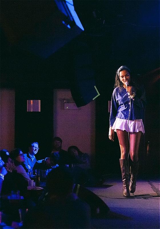 Abby holding a microphone on a stage, a full audience watches her from below.