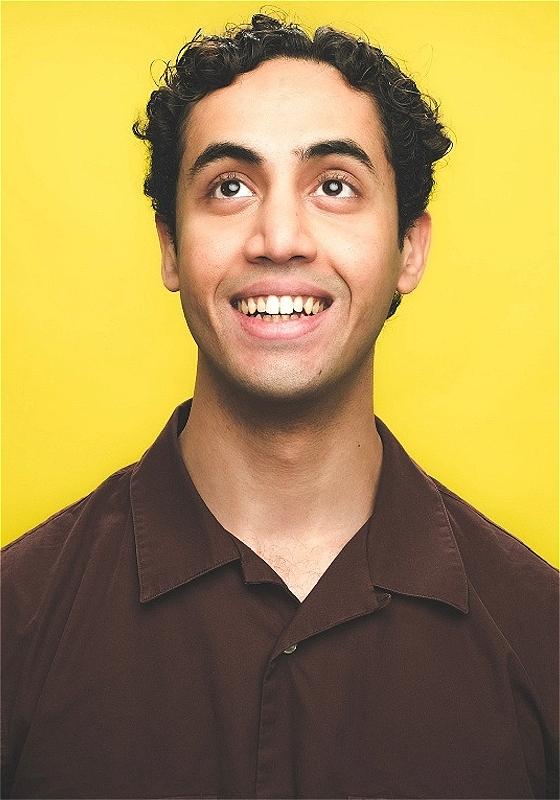 Omar, wearing a brown shirt, smiles up before a yellow background.