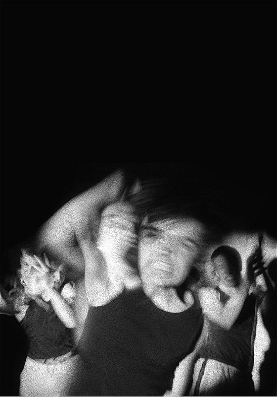 A black and white photo of three men blurred by their movements, before a black background.