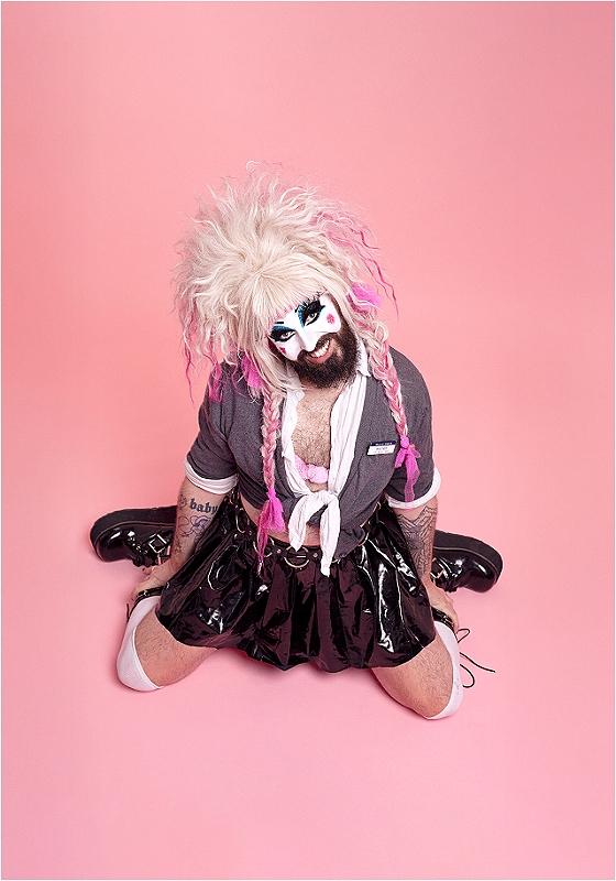 Baby Lame is kneeling on the floor in a very similar pose to the iconic Britney Spears album hit me baby one more time, but with significantly more makeup, more PVC, and bigger hair. Slay. 