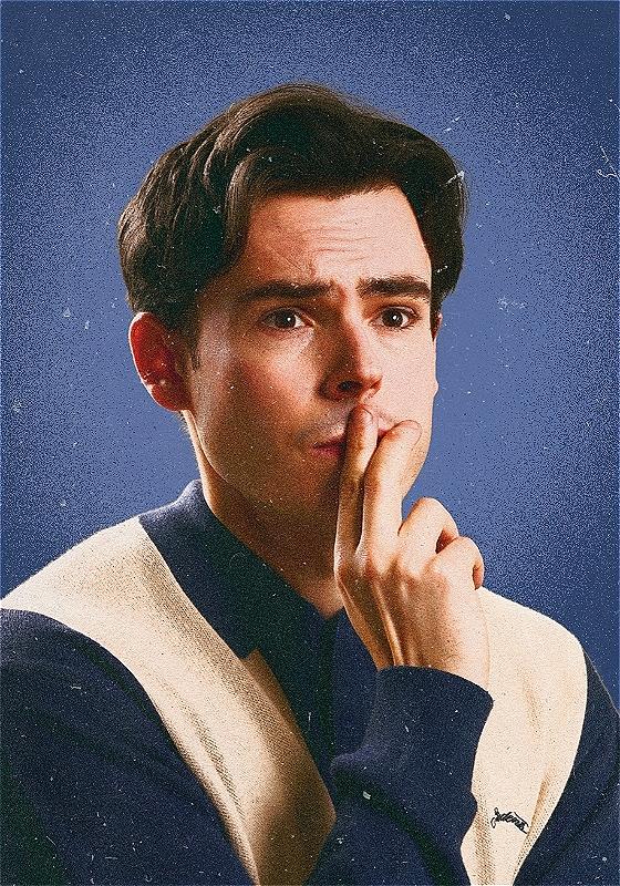 Rhys is holding a hand up to their pursed lips, looking just off-camera. They look worried.