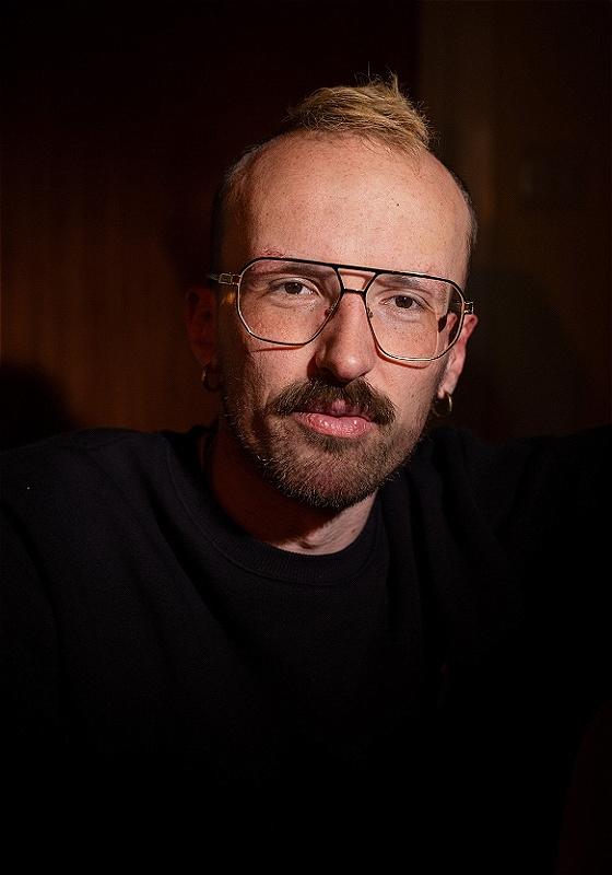 Closeup on andy, who's wearing a dark top against a dark background, and has on some fabulous aviator-style specs