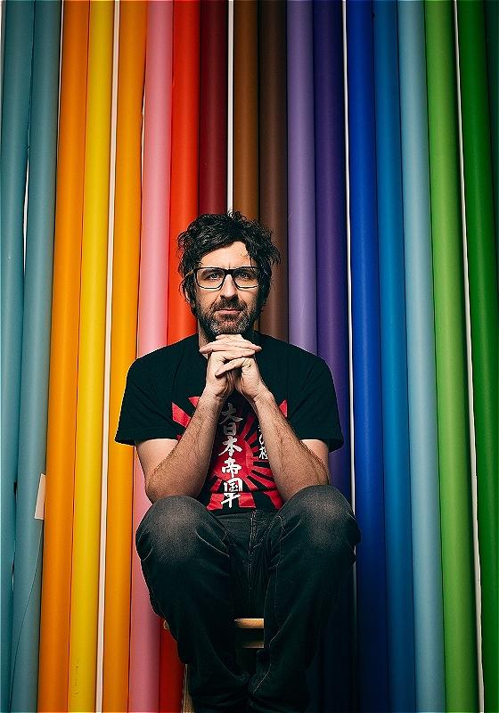 Mar Watson sits with his hands beneath his chin, wistfully staring ahead before a background of multi-colored pool noodles.