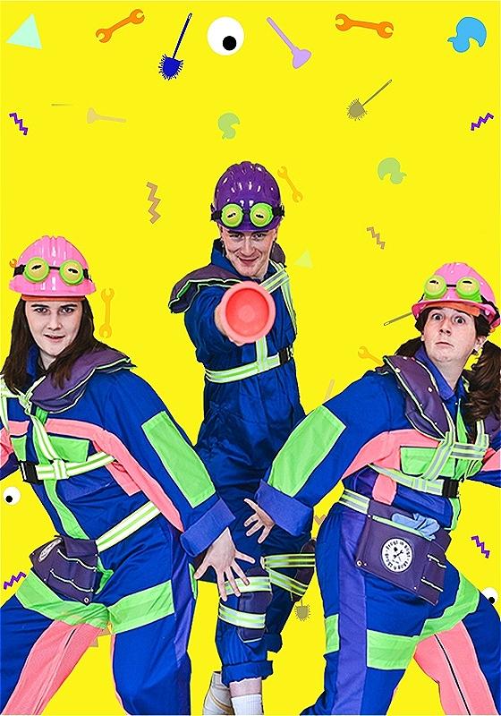 Three people wearing colorful plumber outfits  and colorful helmets with frog eyes stand before a bright yellow background.