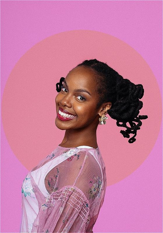 Sharon smiles at the camera before a background of a pink orb and a purple background beyond it.