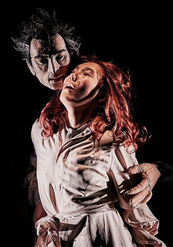 A man stares at a woman from behind as the woman looks up before a black background.