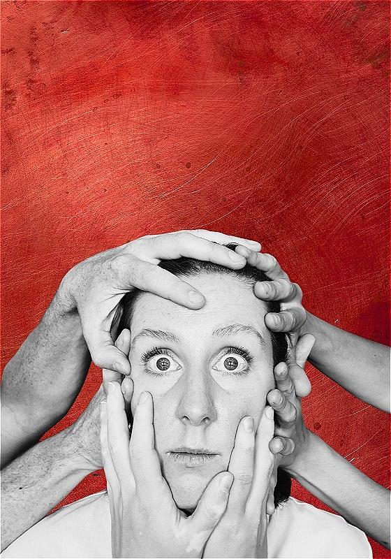 A black-and-white photo of a stunned person who stares ahead as six hands hold their head in place, beyond a red background.