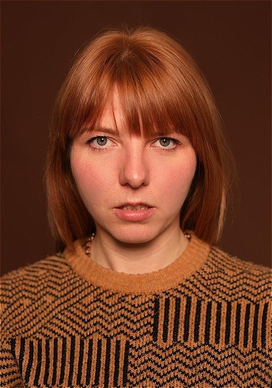 Marty, wearing an orange and black striped sweater, stares ahead before a brown background.
