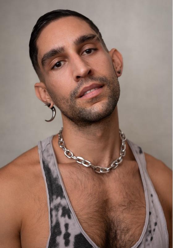 Headshot of Gigi with a large crescent moon shaped earring, chain necklace and a tank top.