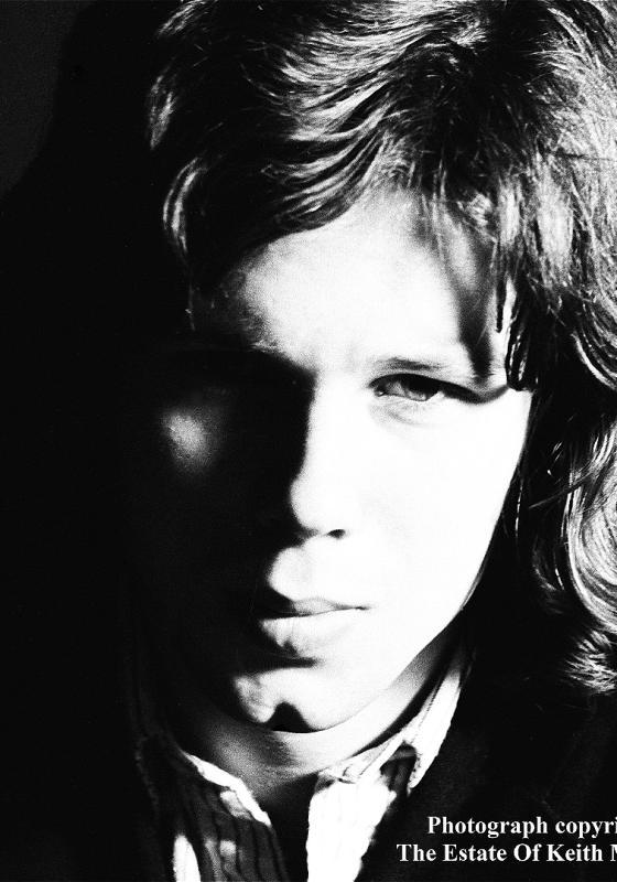 Black and white photo of a young man with shoulder-length hair staring straight ahead. 