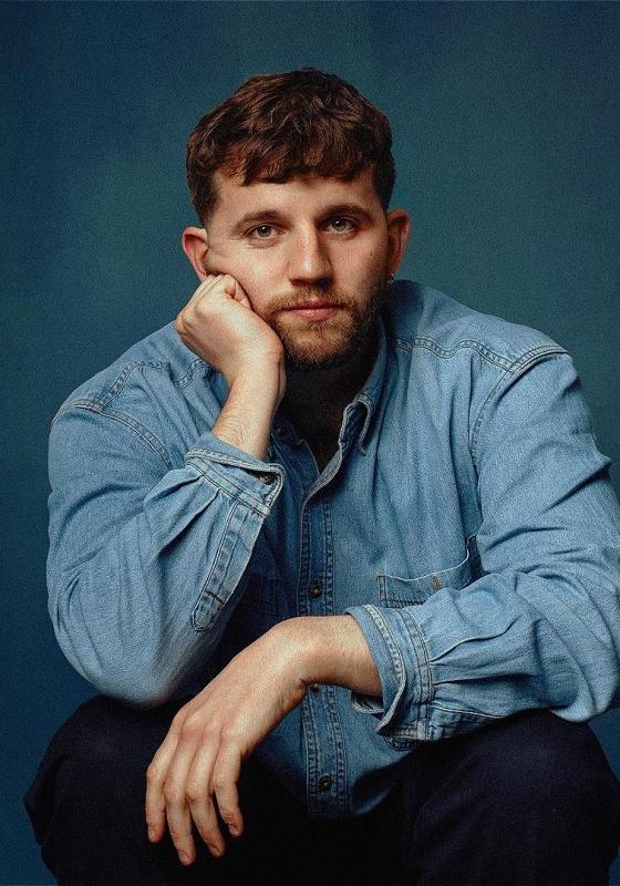 Rory looking into the camera in a blue denim shirt, with a blue background