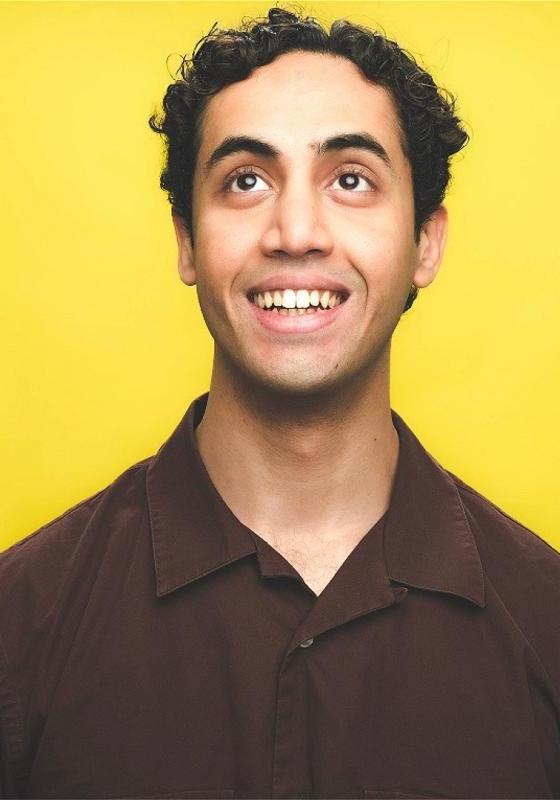 Omar is against a bright yellow backdrop, looking upwards and smiling 