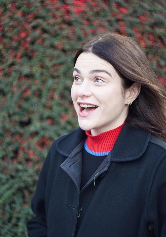 Davina stands outside, wearing a coat and a jumper with a red turtleneck