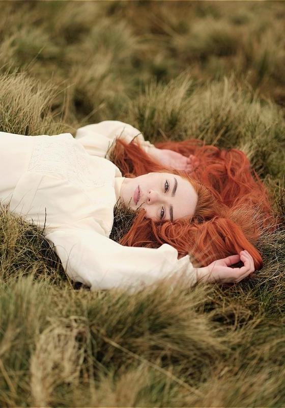 Hannah, wearing a white linen dress, lying down in a field of grass. 