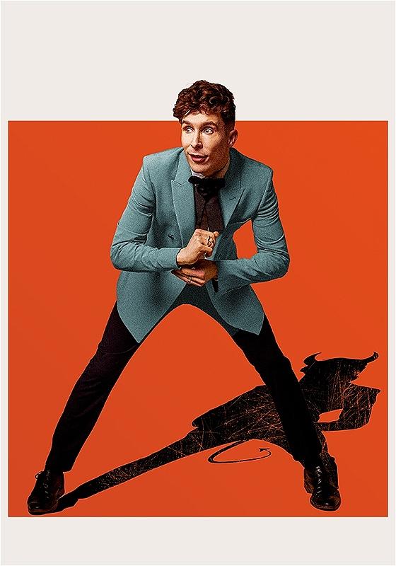 Larry is standing against an orange background, wearing a grey suit jacket and smart black trousers, leans over slightly and fixes a cufflink. Behind him his shadow casts down in the silhouette of a devil. 