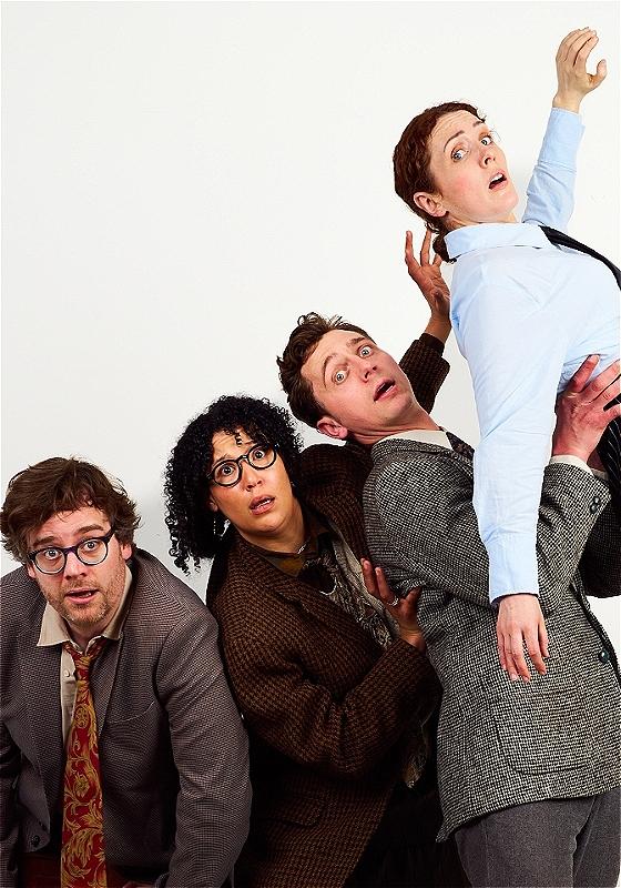 Cast of 4 performers dressed in suits and blazers looking alarmed against a plain white backdrop.