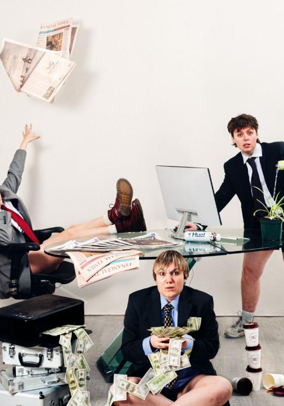 A chaotic scene of three people in suits around a glass desk. On the left is someone shouting on the phone and throwing a newspaper. On the right is someone in front of a computer, watering a plant with an energy drink. Sat on the floor, next to a pile of briefcases, is someone holding a large amount of cash 