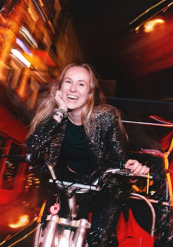 Courtney is riding a rickshaw and smiling at the camera. The street around her is blurry.