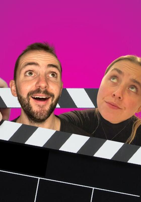 Two people with the heads between a film slate, looking up. They are against a pink background