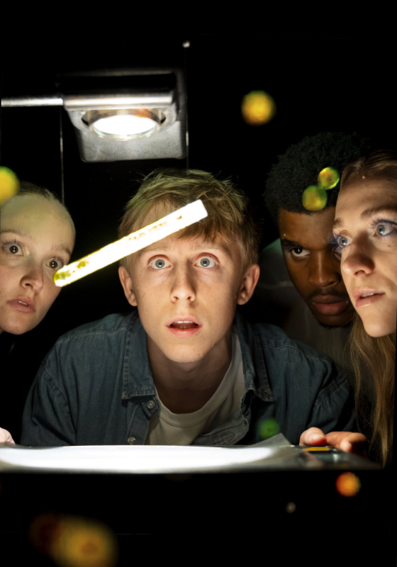 Four people huddle around a test tube in the dark.