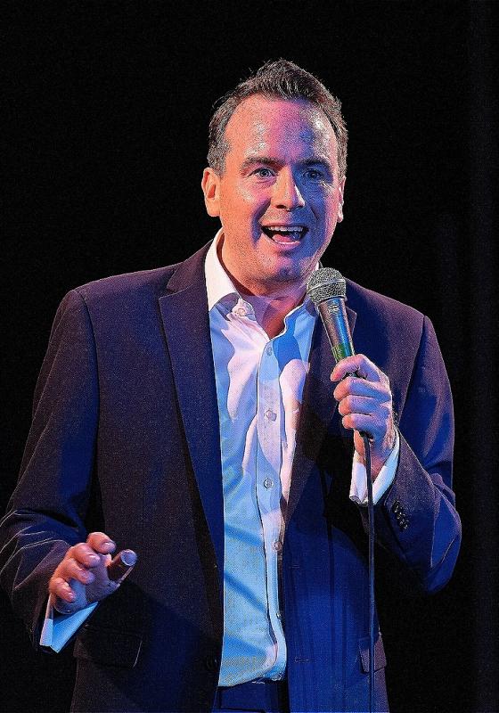 Matt Forde standing on stage holding a microphone 