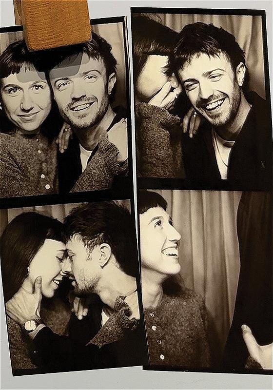 A heteronormative couple take photos in a black and white photobooth. They appear to be in love, and are laughing.