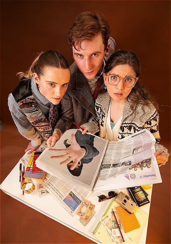 A vintage-looking scene of three people gathered around a table. The three individuals are leaning in closely and looking upward toward the camera with slightly concerned expressions. On the table there are various items including an open newspaper, a magazine and passports.