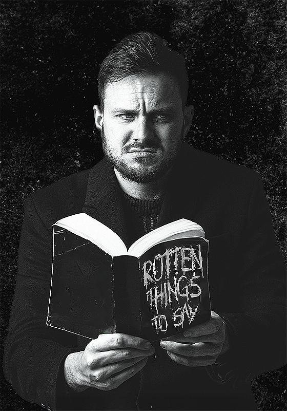Black and white image of Mike grimacing while holding a book titled 'Rotten things to say'