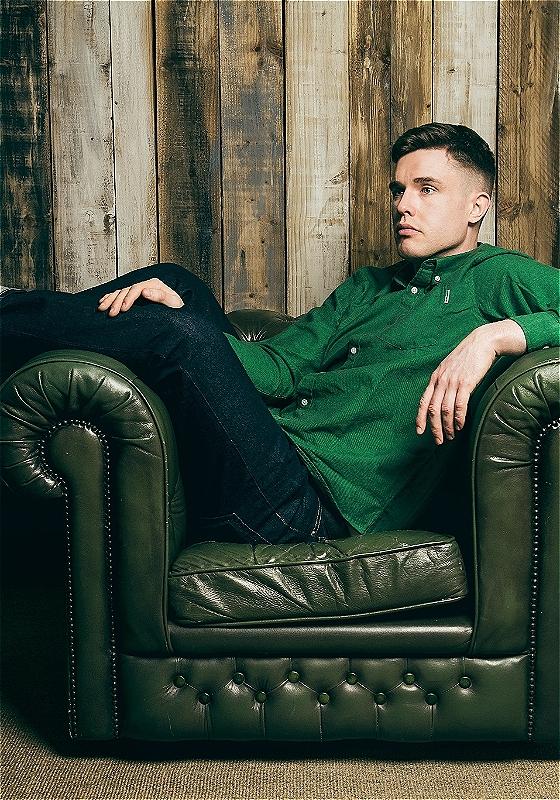 Ed Gamble lounging on a green leather armchair staring into the distance with a forlorn expression on his face.