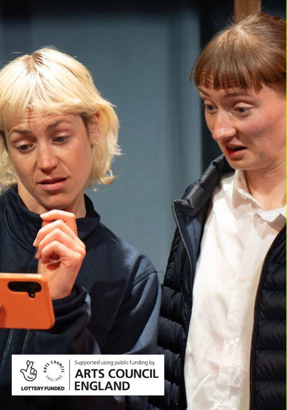 Two performers looking at a phone with a perplexed but intrigued expression on their face