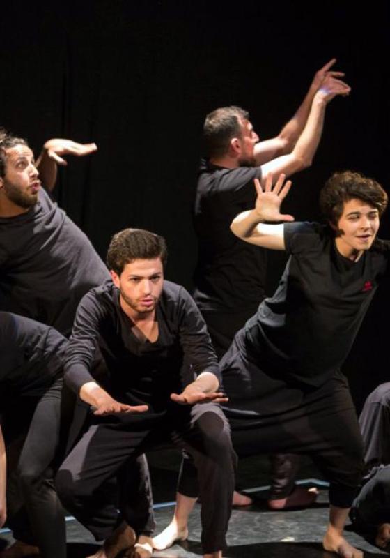 Six performers in dark clothing strike expressive, theatrical poses.
