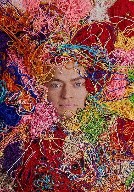 Man hidden in colourful threads with only his face showing