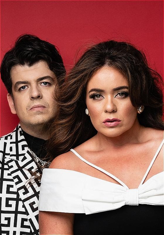 The performers serving face to the camera against a red background