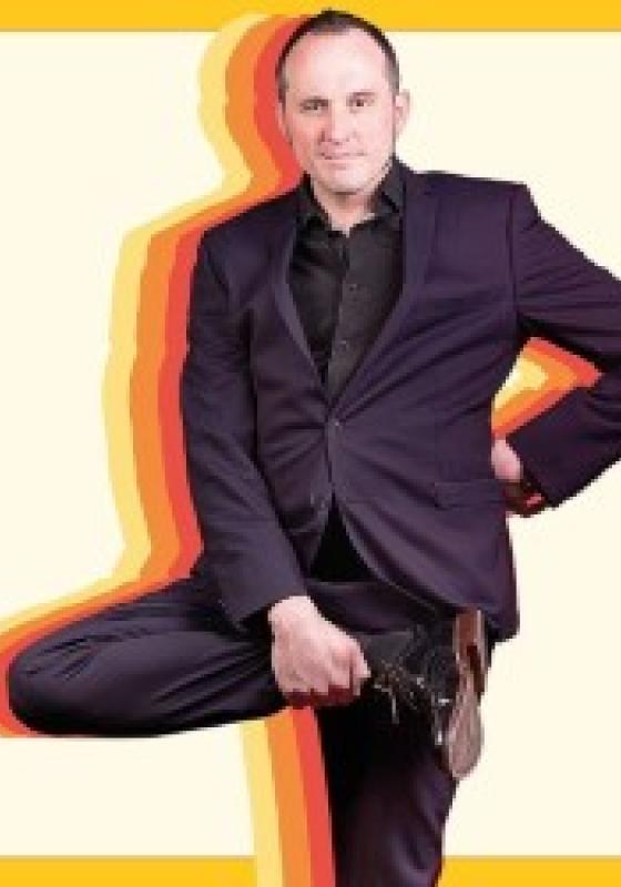 Phil looks into the camera whilst holding up their right foot. Behind them are colourful silhouettes. A