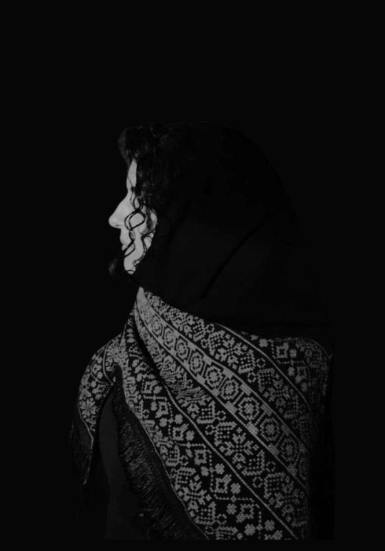 A black and white image of a woman's side portrait, with a traditional shawl on her shoulders
