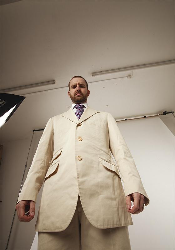Rob Preston wearing a cream suit from an extreme low-angle shot to accentuate his power