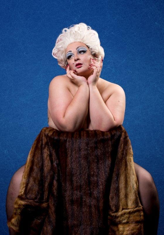 Mitzi Fitz sitting naked on a chair draped in a fur coat looking pensively into the distance
