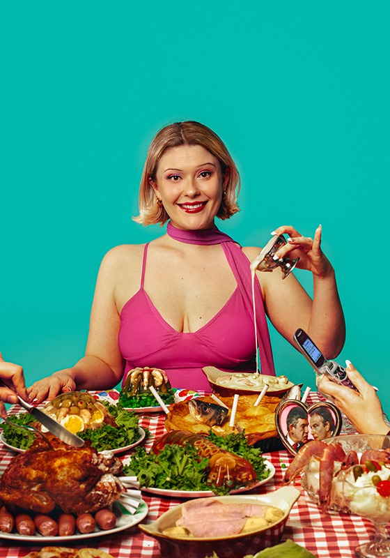 A woman dressed in pink sits at the head of a table filled with large portions of food.