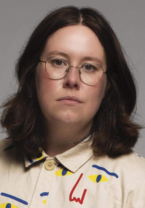 Chloe with a blank expression, wearing a shirt with an artistic pattern. 