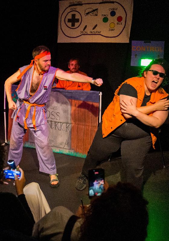 A performer dressed in a karate uniform mid punch whilst someone winces in pain.
