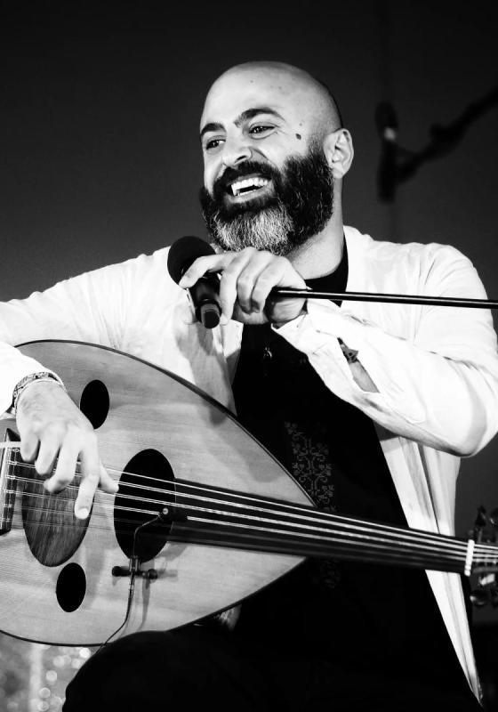 A black and white image of Saied sits behind a musical instrument in front of a microphone